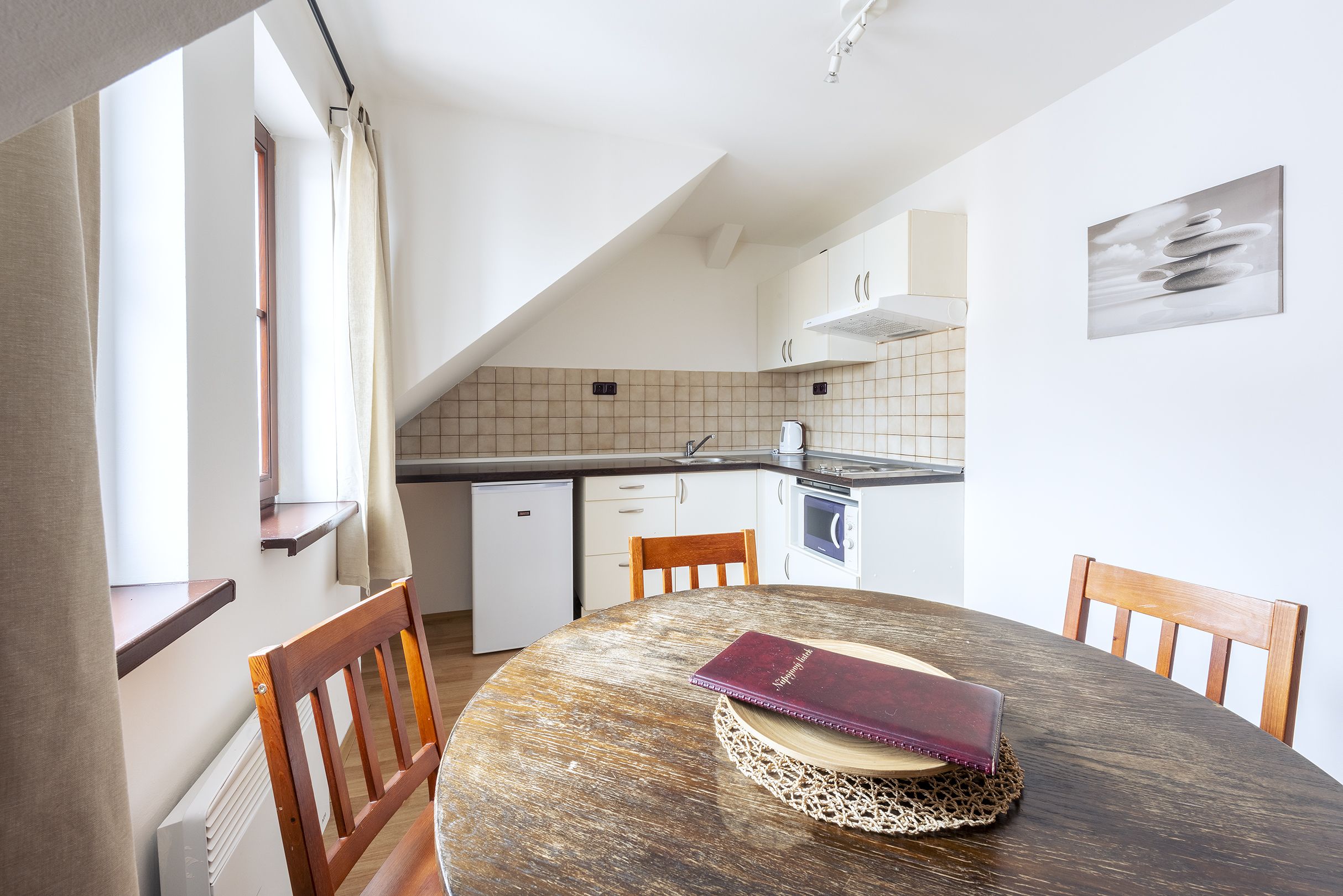 A kitchen with a dining table, chairs, a book, and a small refrigerator.