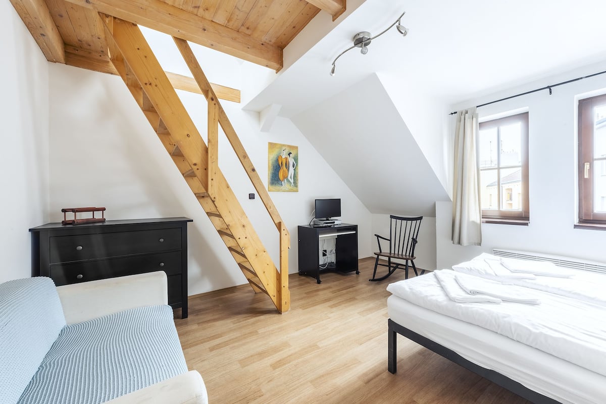 A bedroom with a sloped ceiling, a bed, a desk, a chair, and a painting on the wall.