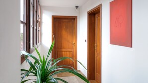 Un couloir avec une porte en bois, une plante en pot et une œuvre d’art rouge accrochée au mur.