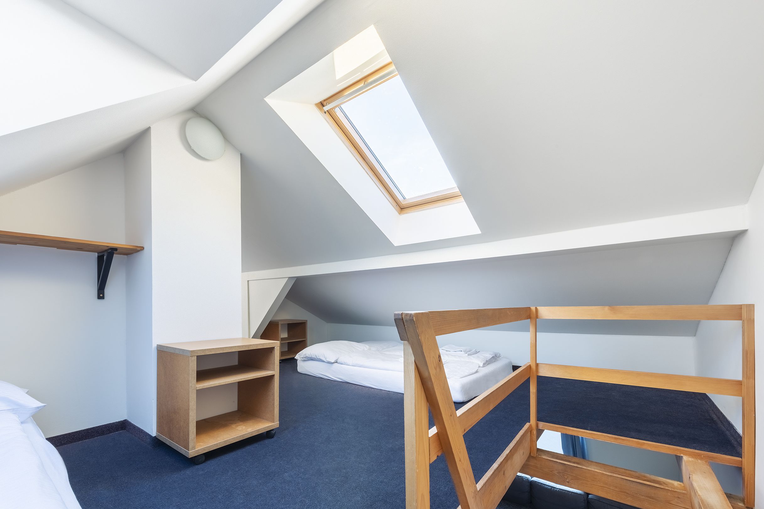 Habitación compacta y moderna con techo inclinado, tragaluz, litera, estante de madera pequeño y mesita de noche.