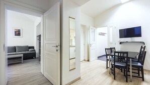 Un salon moderne comprenant un canapé, une table à manger avec des chaises, un téléviseur fixé au mur et une porte donnant sur une autre pièce.