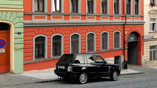 Un immeuble à plusieurs étages, doté d’une façade rouge, de nombreuses fenêtres et d’une voiture garée devant.