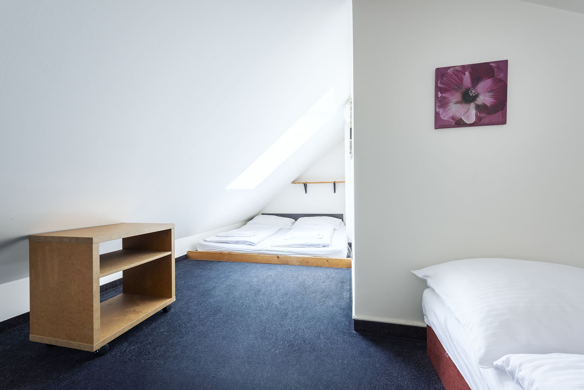 A small, tidy room with a bunk bed, a wooden shelf, and a single flower painting on the wall.