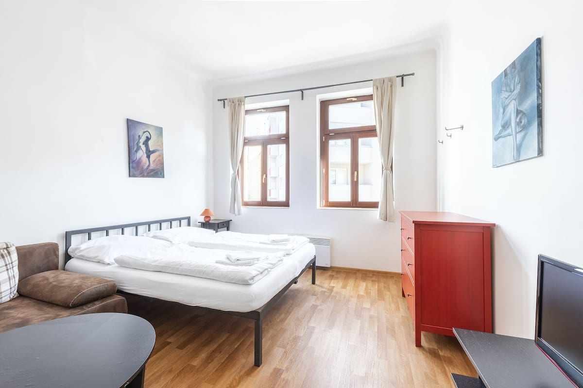 A bedroom with a bed, a desk, a red cabinet, and a TV.