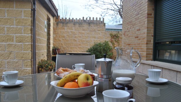 Una mesa de desayuno con un bol de fruta, cafetera y tazas.