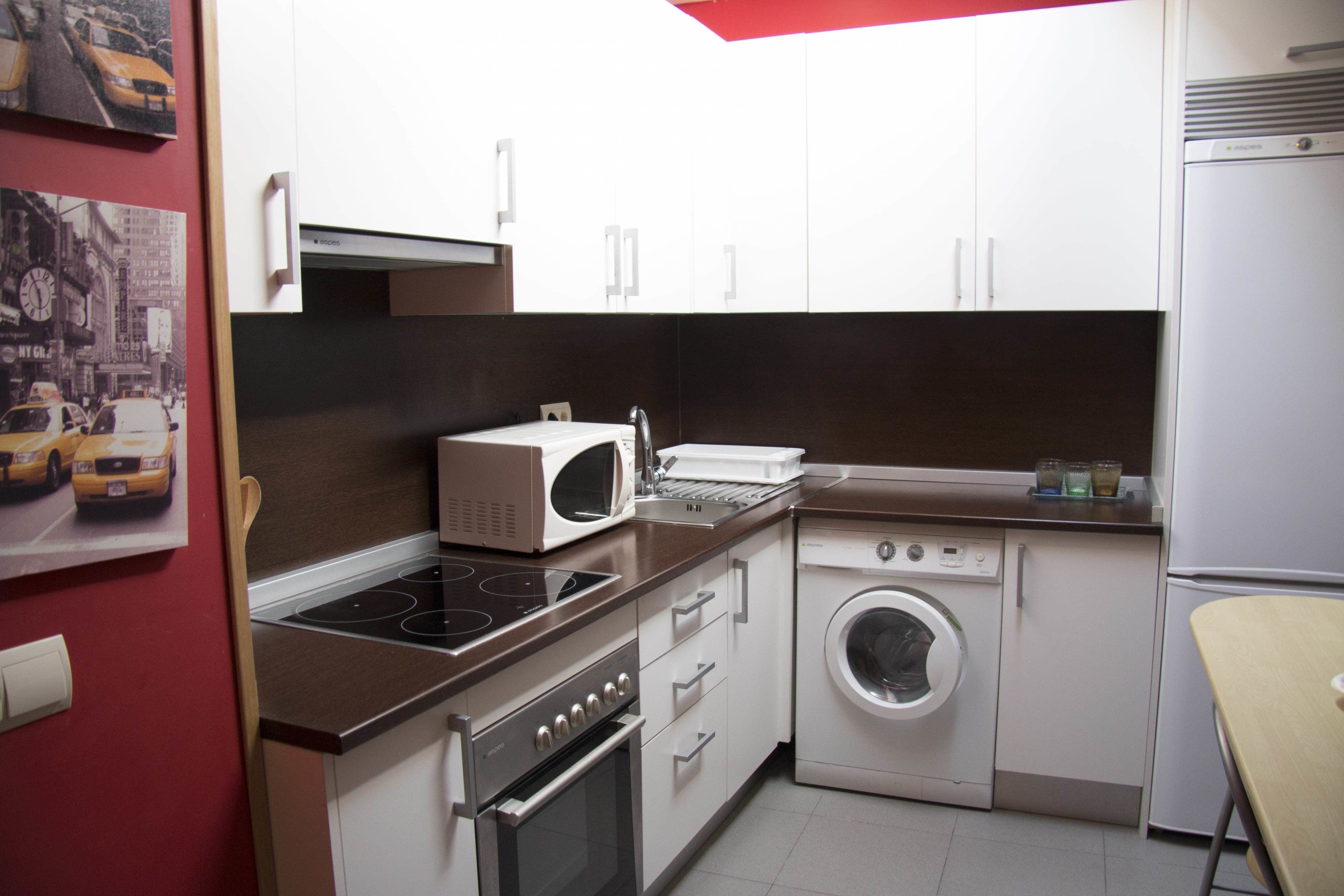 Una cocina compacta con armarios blancos, microondas, estufa, lavadora y una pequeña mesa.