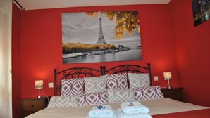 Una cama con una pared roja, un cuadro de la Torre Eiffel, almohadas estampadas y dos lámparas de noche.