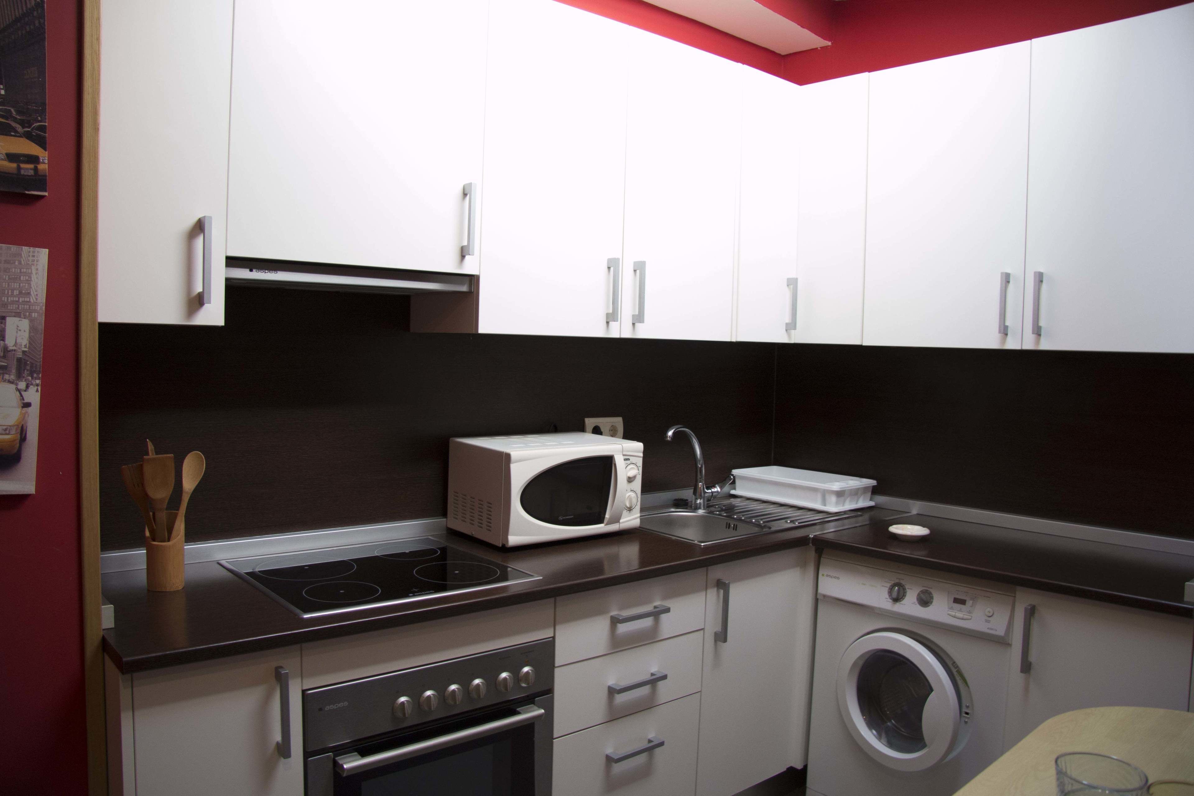Cocina compacta con armarios blancos, microondas, horno y lavadora.