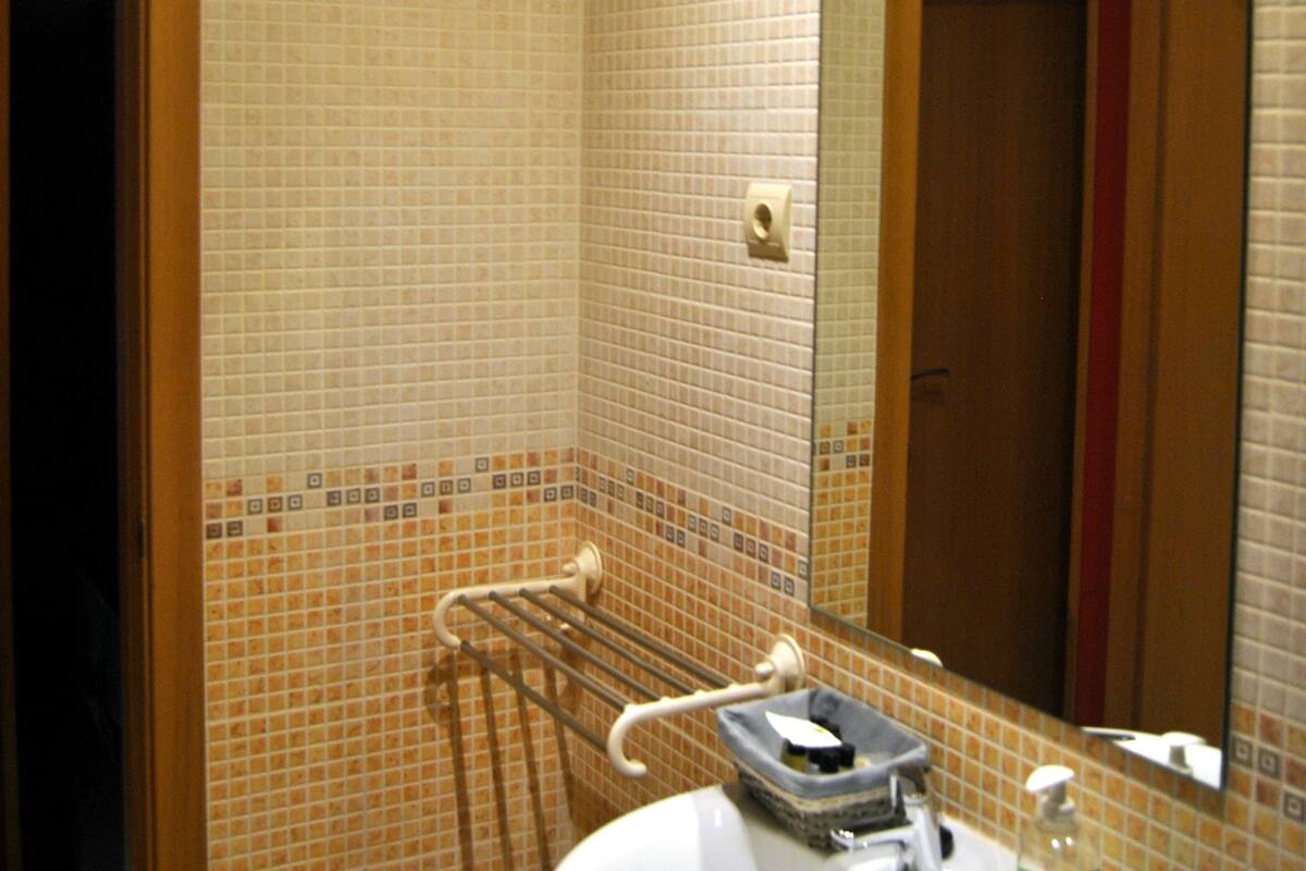 A bathroom with a tiled wall, a sink with a mirror, and a towel rack.