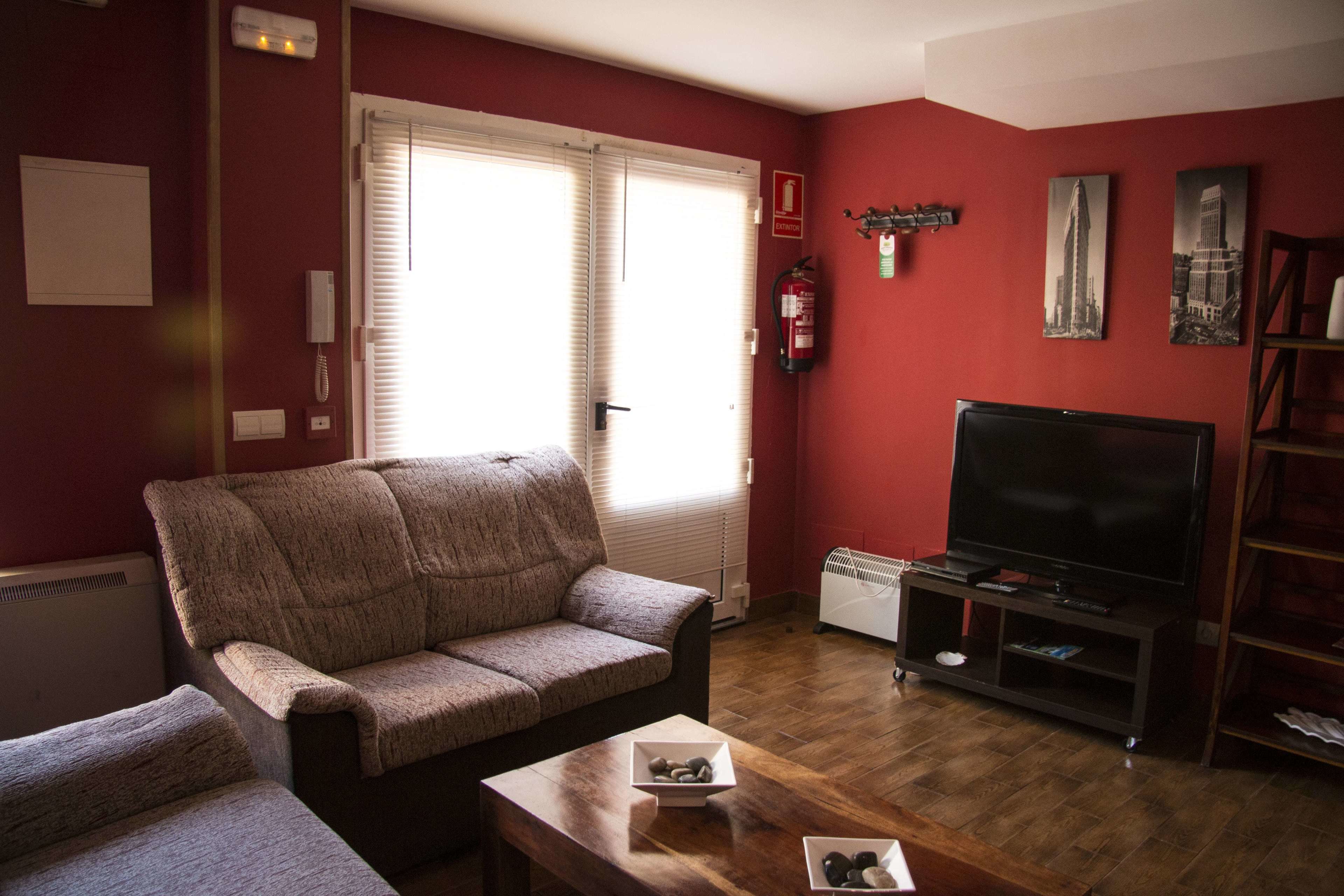 Una sala de estar con un sofá, un televisor en un mueble bajo, una mesita con un cuenco y una estantería.