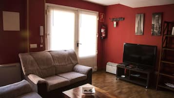 Una sala de estar con un sofá, un televisor en un mueble bajo, una mesita con un cuenco y una estantería.