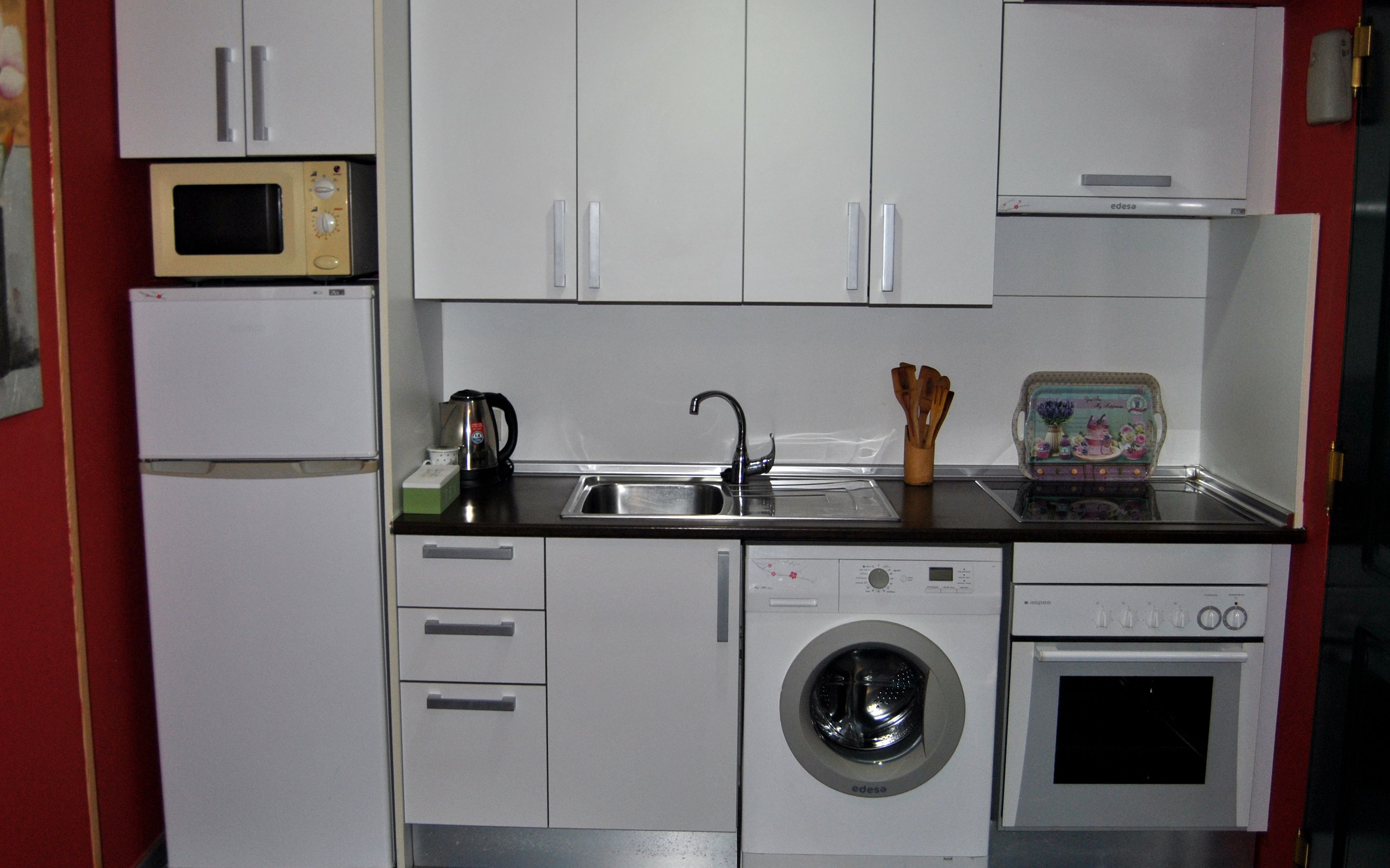 Una cocina compacta con microondas, lavaplatos, hervidor y lavadora.