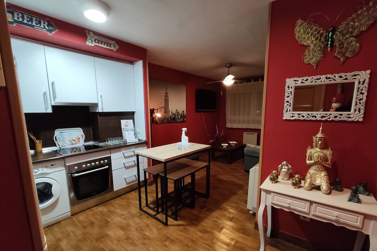 A compact kitchen with a dining area, a washing machine, and a small table with decorative items.