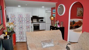 Una sala de estar con un sofá color beige, un comedor con una mesa blanca y una cocina con gabinetes blancos.