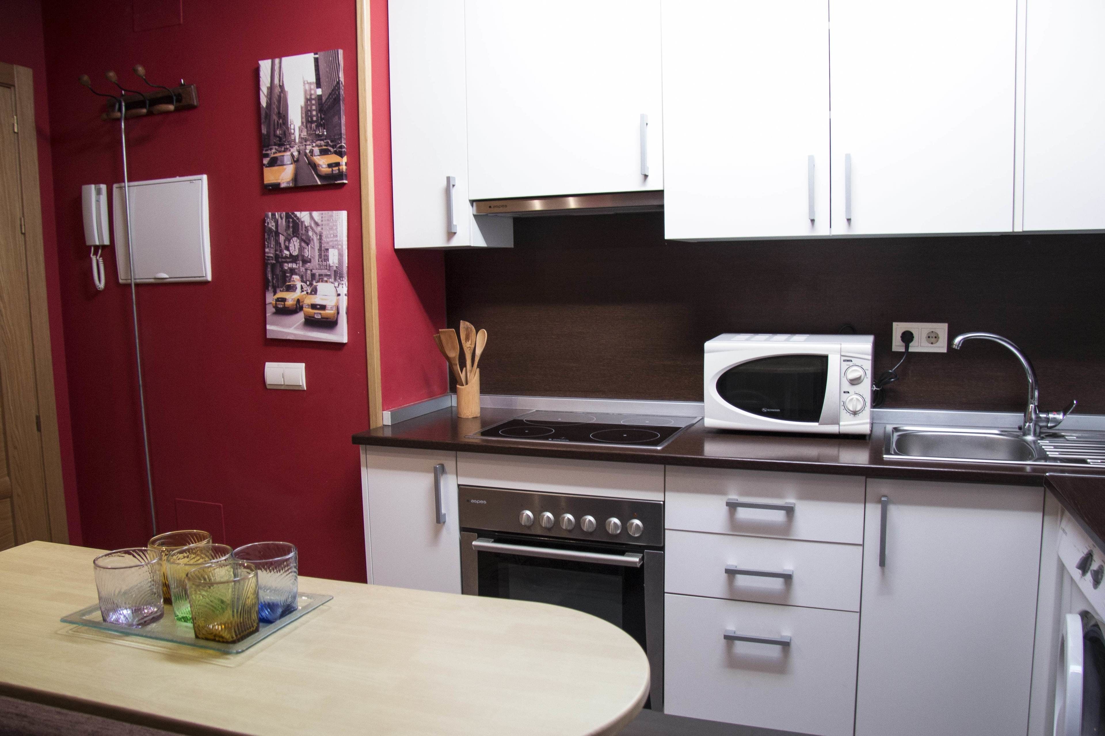 Een keuken met witte kasten, een magnetron, een fornuis en een spoelbak. Er hangen ingelijste foto's aan de muur en op het aanrecht staat een dienblad met glazen.