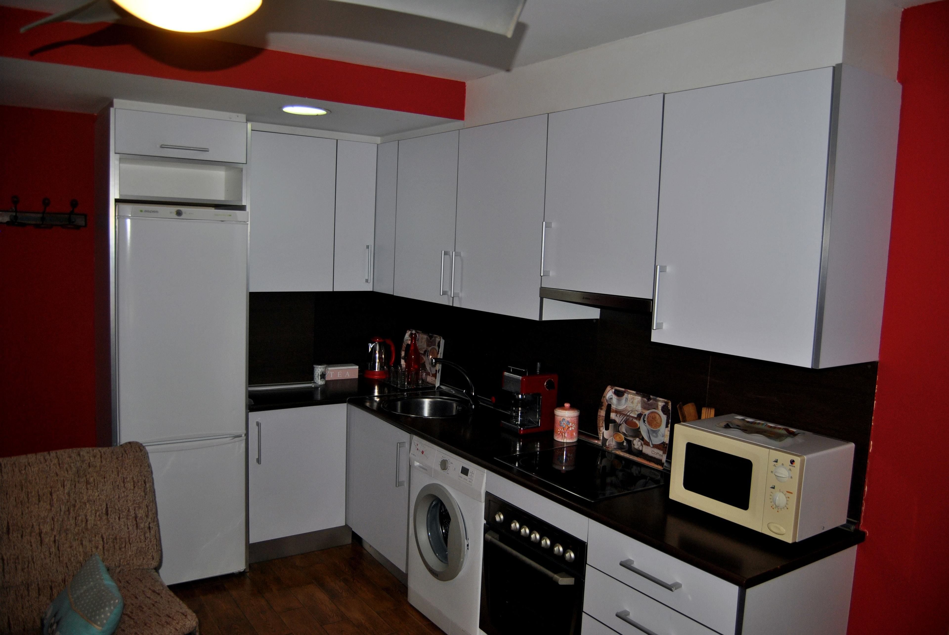 A compact kitchen with white cabinets, a washing machine, a microwave, and a sink.