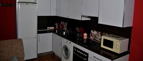 A compact kitchen with white cabinets, a washing machine, a microwave, and a sink.