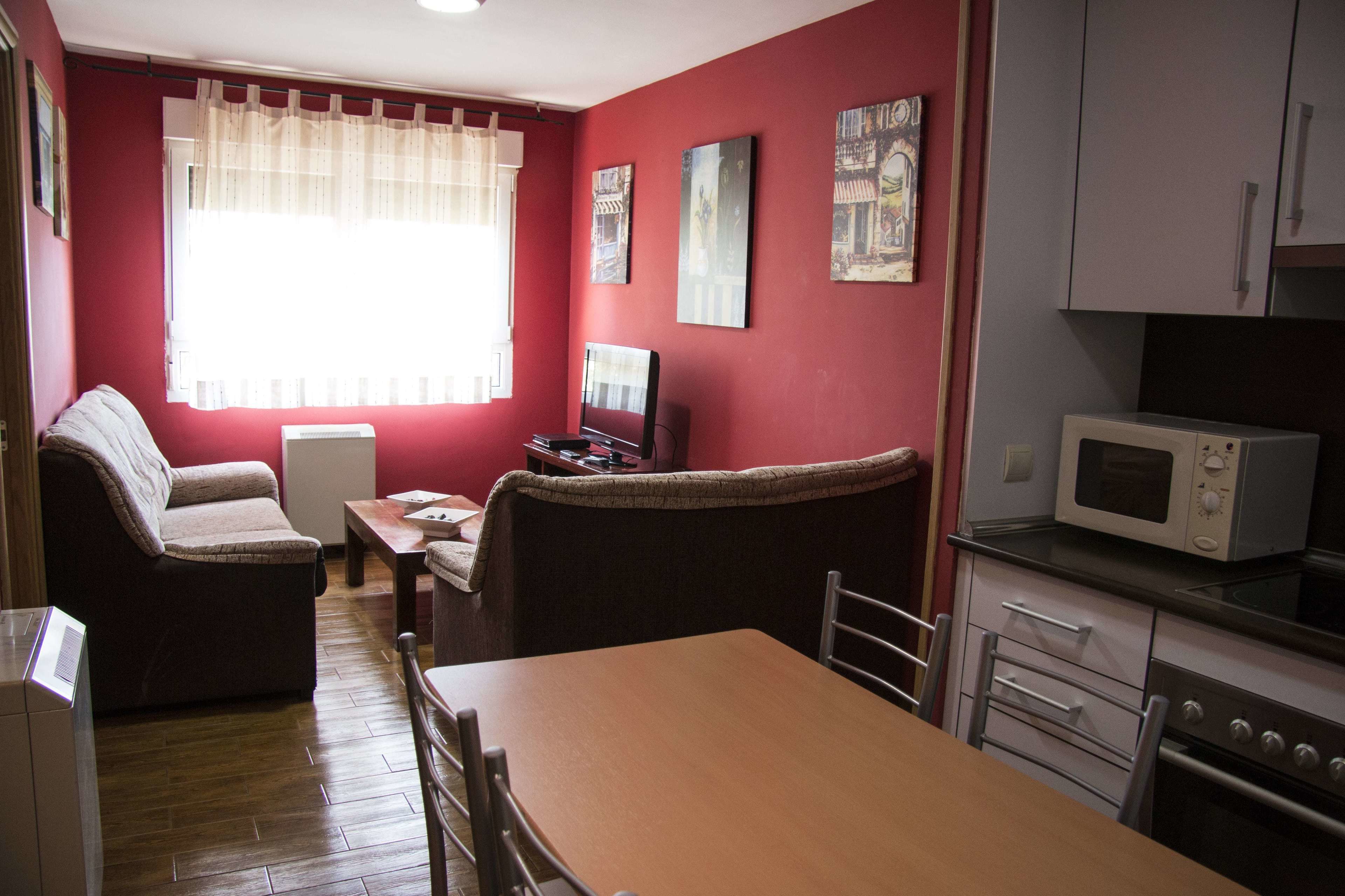 Ein gemütlicher Wohnbereich mit Sofa, Esstisch, Fernseher und einer Küchenzeile mit Mikrowelle und Backofen.