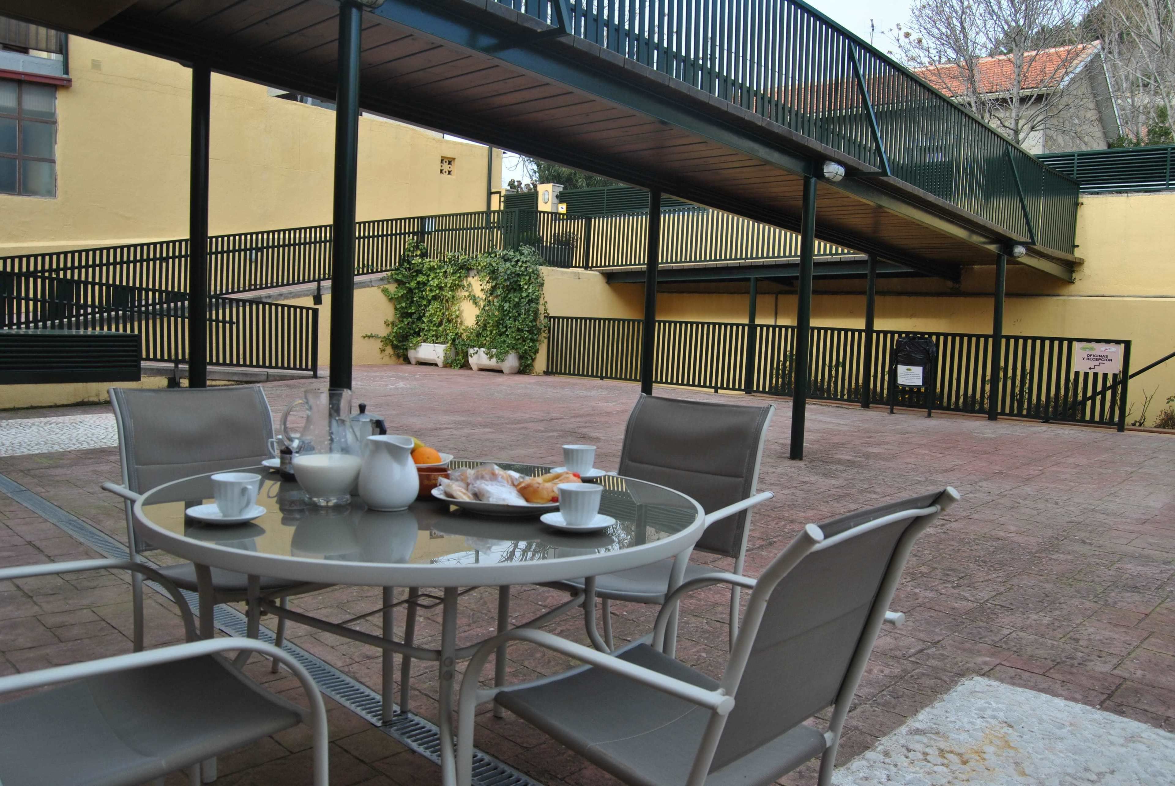 A patio with a round table set for breakfast, surrounded by chairs, and a covered walkway above.