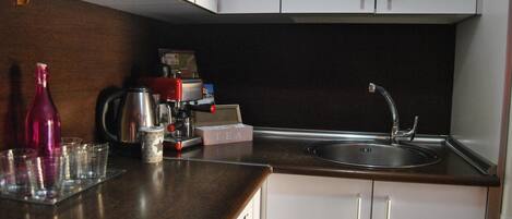 Una cocina con encimera oscura, armarios blancos, un lavamanos de acero inoxidable y una cafetera.