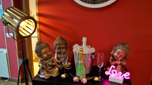 Una estatua de Buda, una botella de champán y un letrero de neón sobre una mesa negra frente a una pared roja.