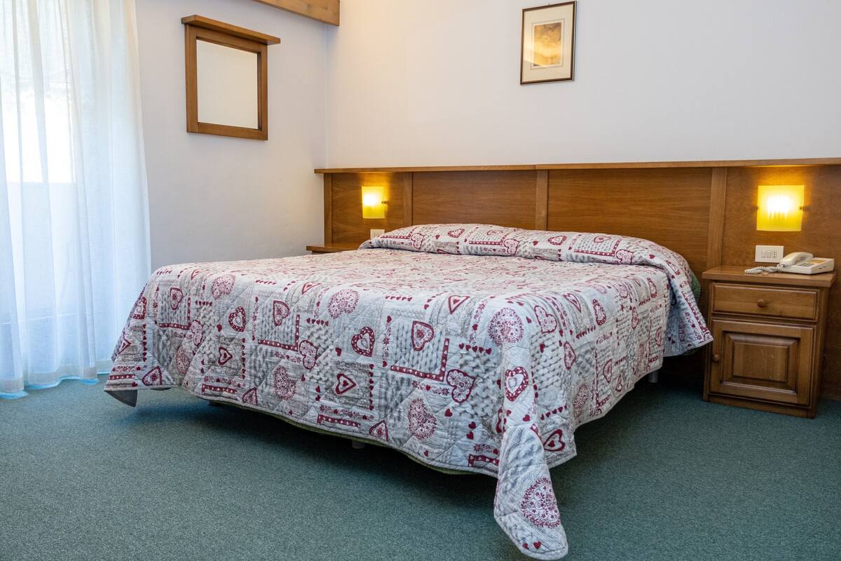 Un lit bien fait, recouvert d’une couvre-lit à motifs, une lampe de chevet et une table de chevet avec un téléphone.