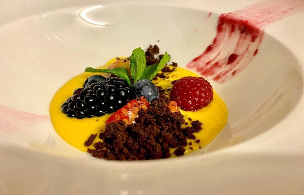 A dessert with berries and a mint leaf on a plate.