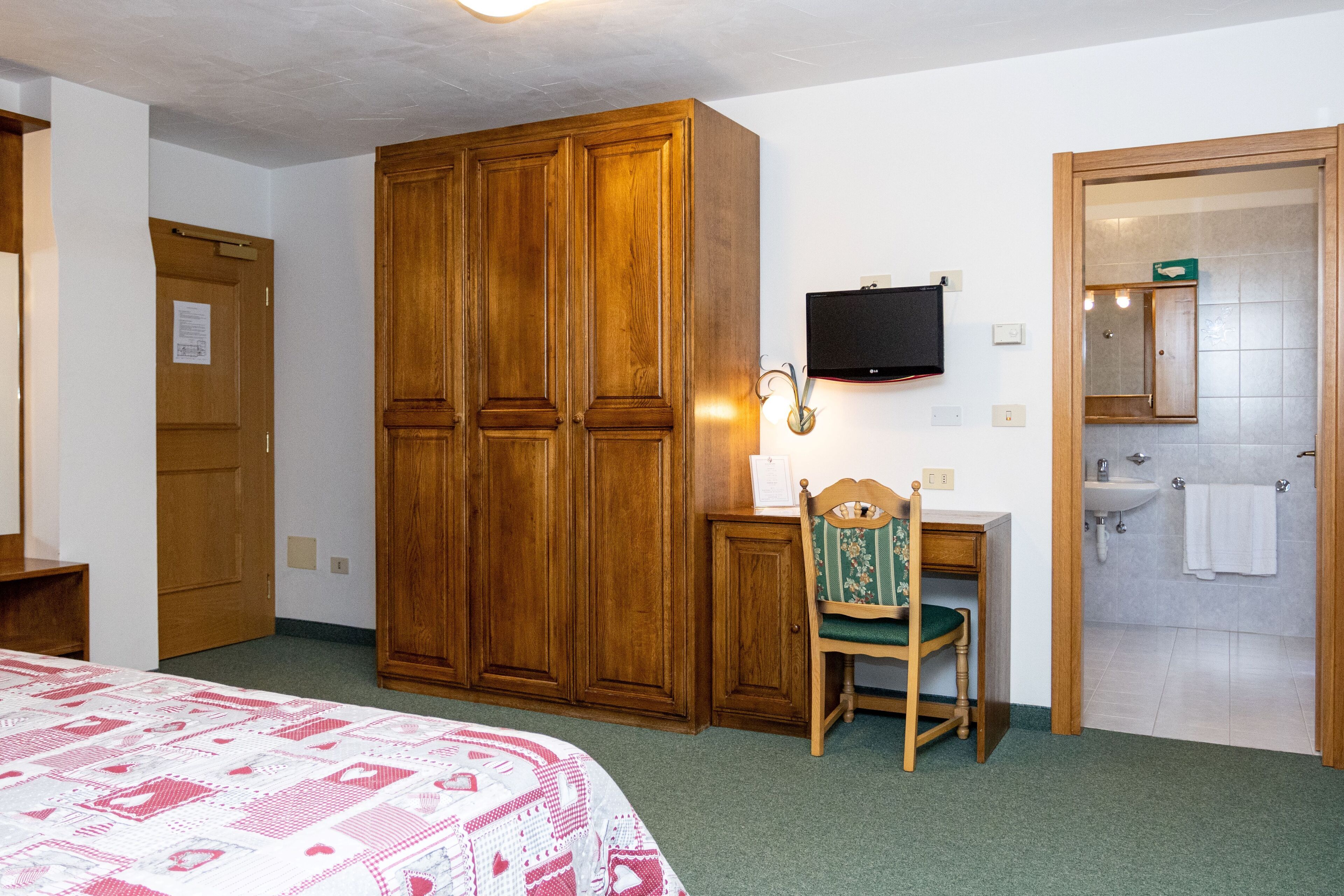 A bedroom with a bed, wooden wardrobe, desk with chair, TV, and bathroom.