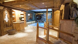 A spa area with a stone floor, wooden railings, and a large stone wall. - Wellness Hotel Dolomia (Soraga)