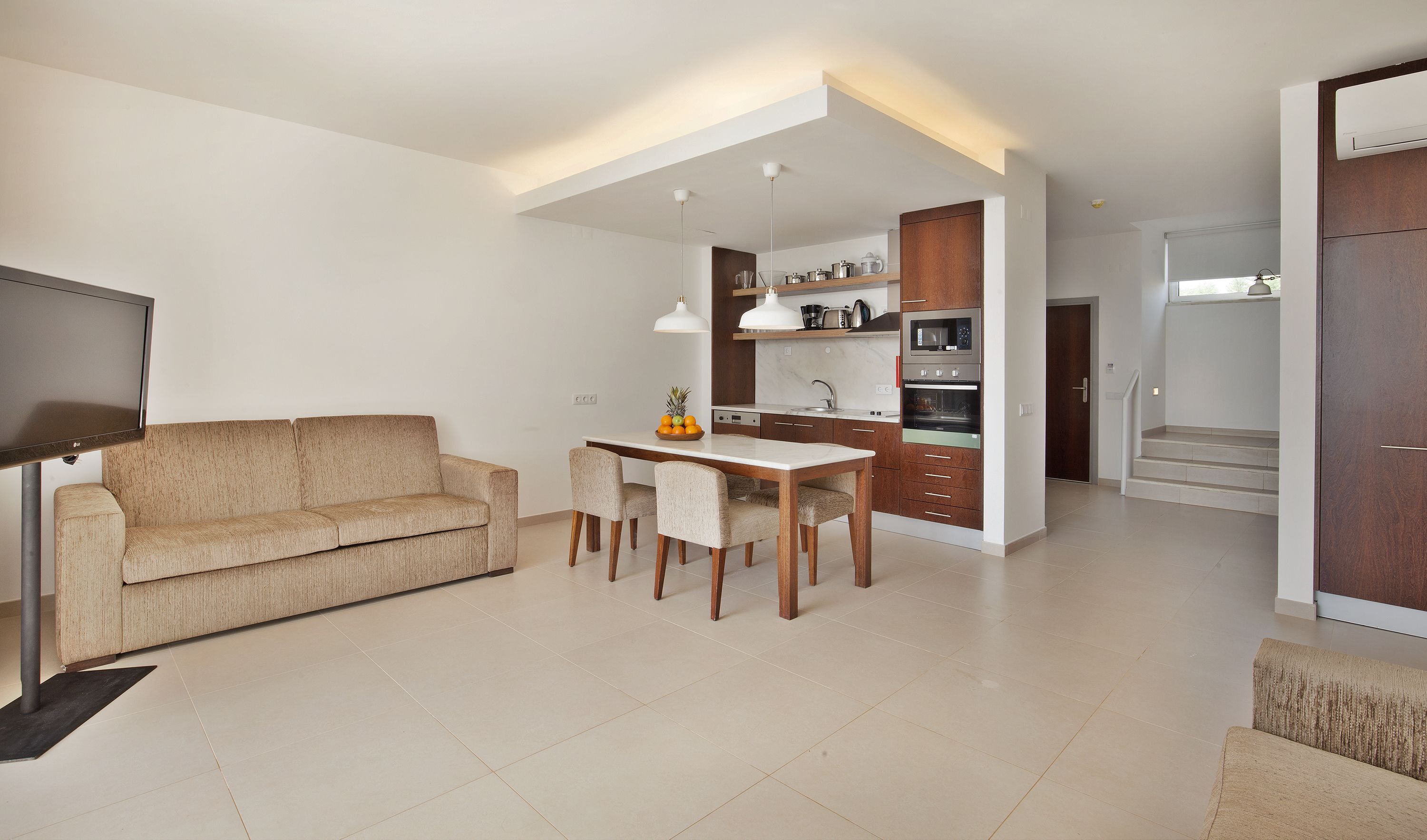 A modern living room with a sofa, dining table, and chairs. There is a kitchen area with cabinets, a microwave, and a coffee maker.