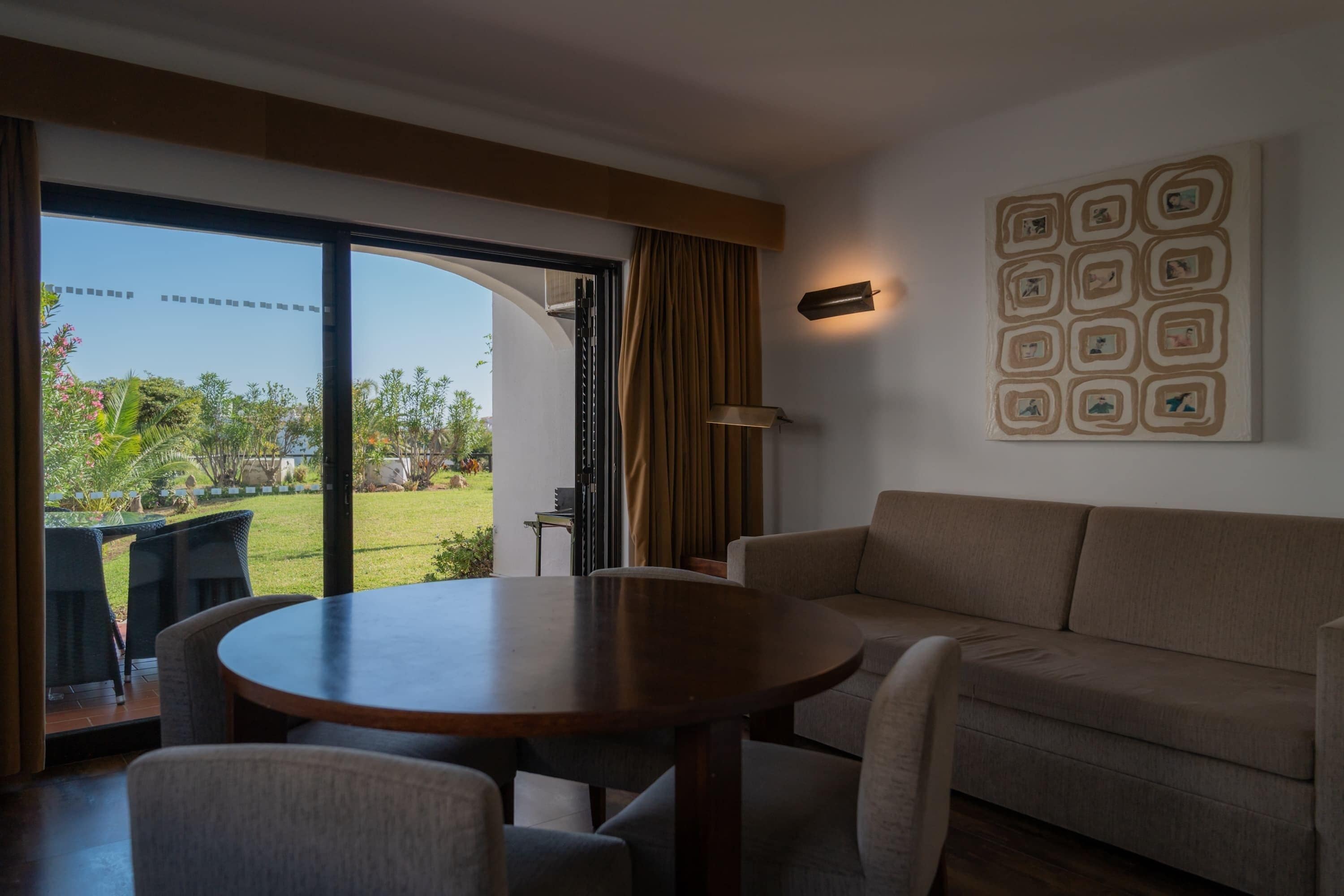 Un salon moderne avec une table ronde, un canapé et une grande fenêtre donnant sur un jardin.