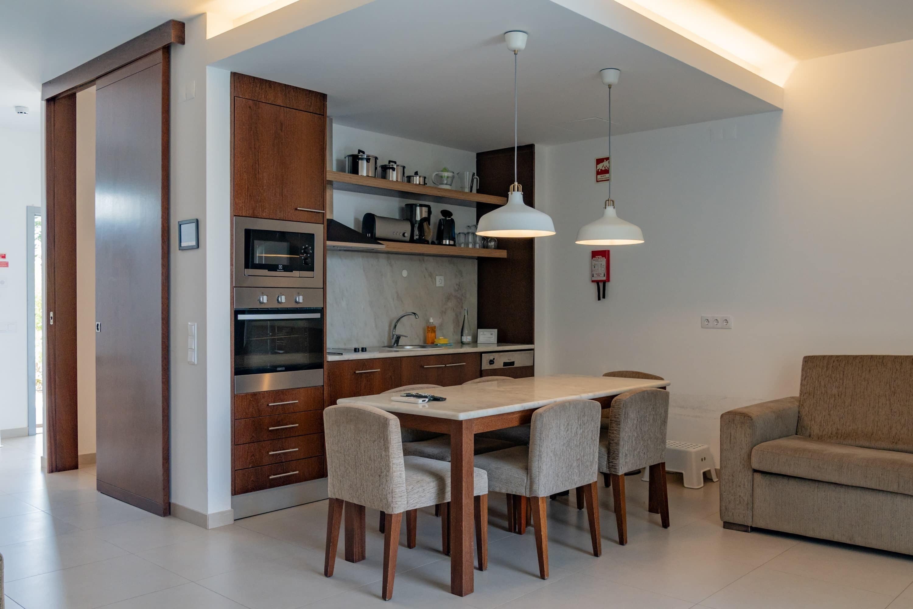 Una cocina moderna con armarios de madera, horno integrado y comedor con mesa y sillas.