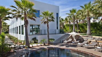 Un edificio moderno con piscina, palmeras y sillones de descanso.