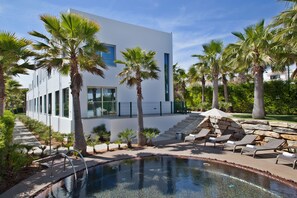 A modern building with a pool, palm trees, and lounge chairs.