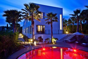A modern building with a pool, palm trees, and outdoor seating.