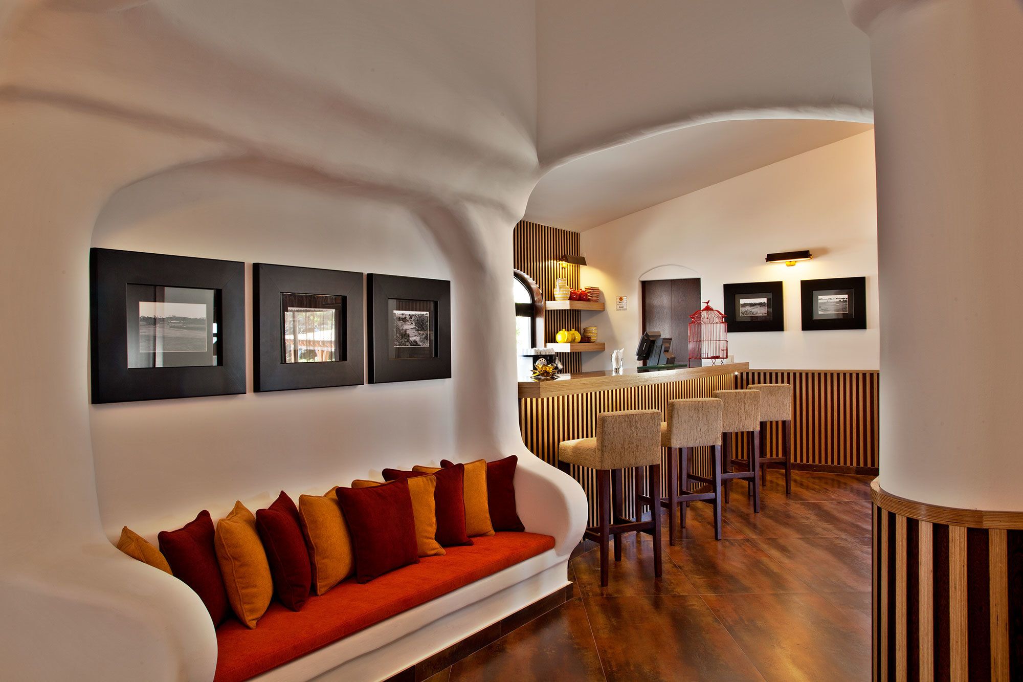 Un intérieur moderne avec un canapé blanc aux lignes courbes, un coin bar en bois et des tableaux encadrés accrochés aux murs.