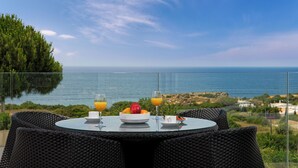 A dining table with a fruit bowl, two glasses of orange juice, and a cup, set against a scenic ocean view. - São Rafael Holidays (Albufeira)