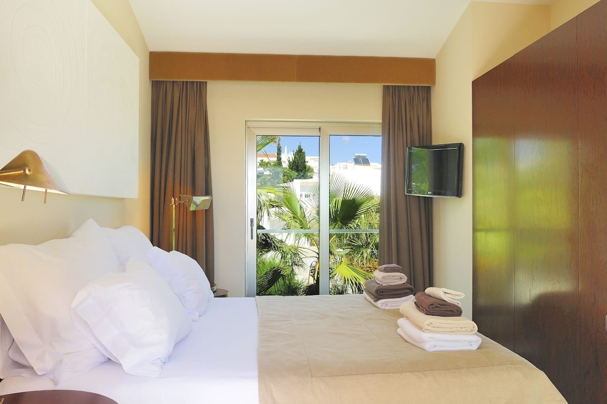 Habitació d'hotel amb llit, televisió de pantalla plana, balcó amb cortines i vistes a palmeres.