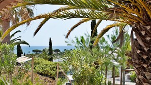 A covered outdoor area with a view of the sea, palm trees, and a grassy lawn. - São Rafael Holidays (Albufeira)