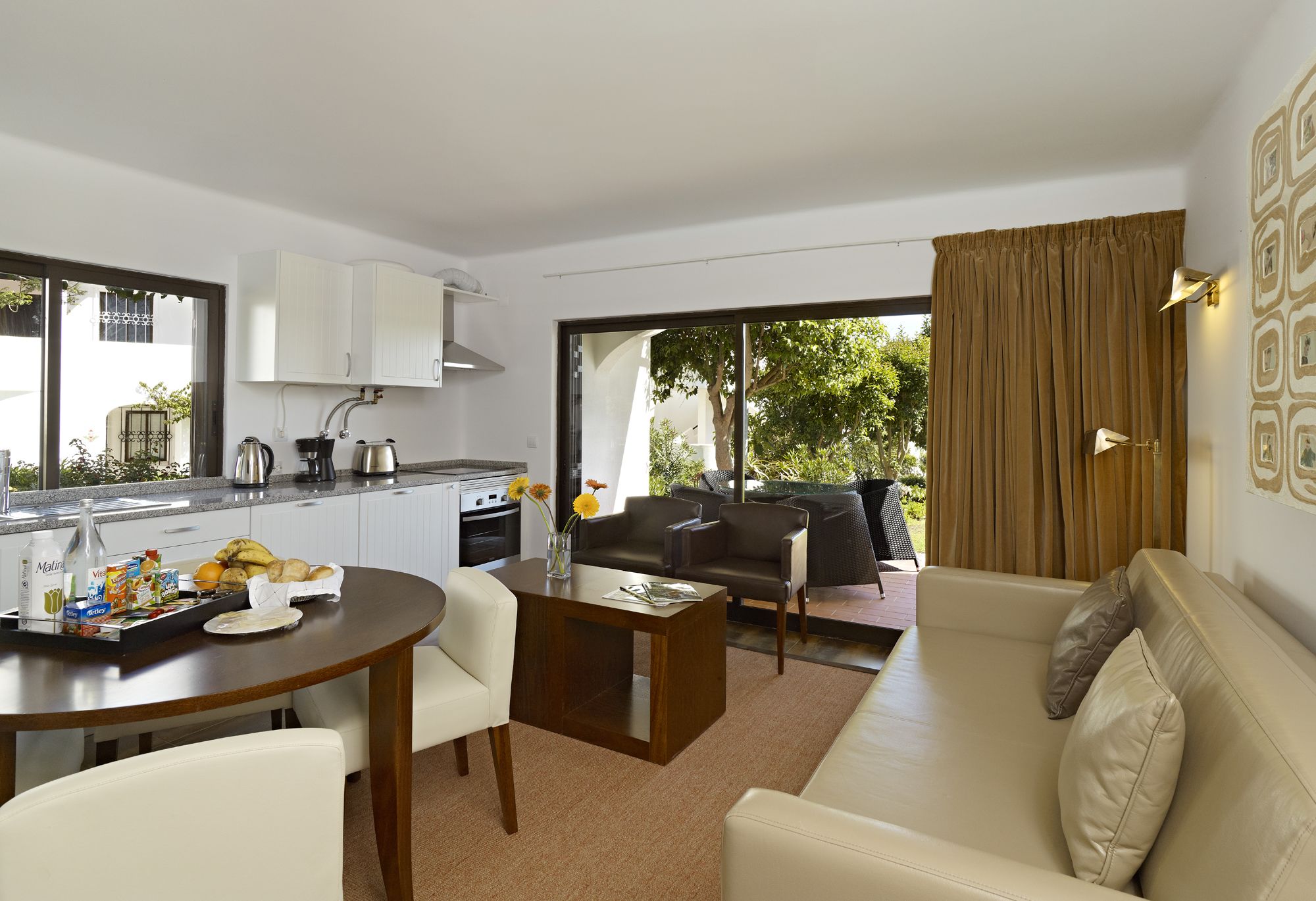 A modern living room with a sofa, a dining table, and a kitchen area with cabinets and a coffee machine.