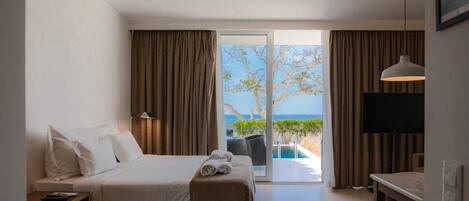 A hotel room with a bed, a desk, a TV, and a view of the ocean.
