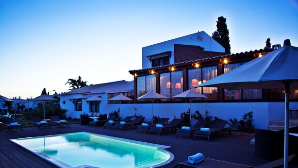 A pool area with lounge chairs and umbrellas, a building with a white facade and red roof, and a clear sky. - São Rafael Holidays (Albufeira)