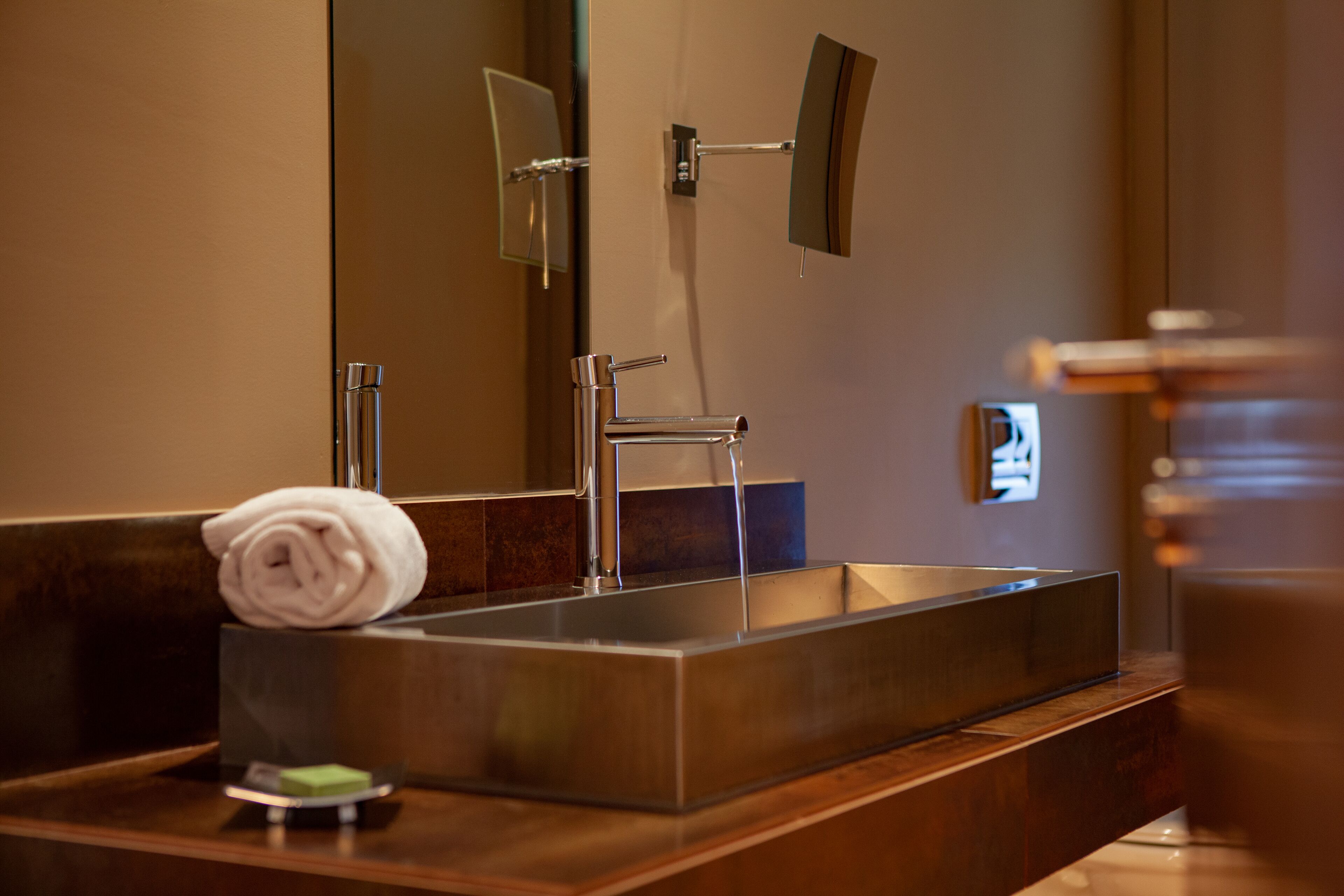 Un baño moderno con un lavamanos de acero inoxidable, una toalla y un espejo.