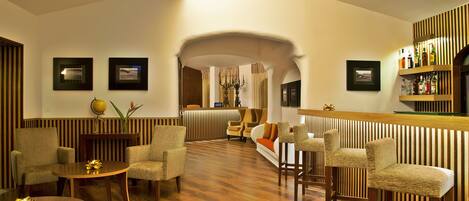 A hotel lobby with a wooden floor, striped walls, a reception desk, and seating areas.