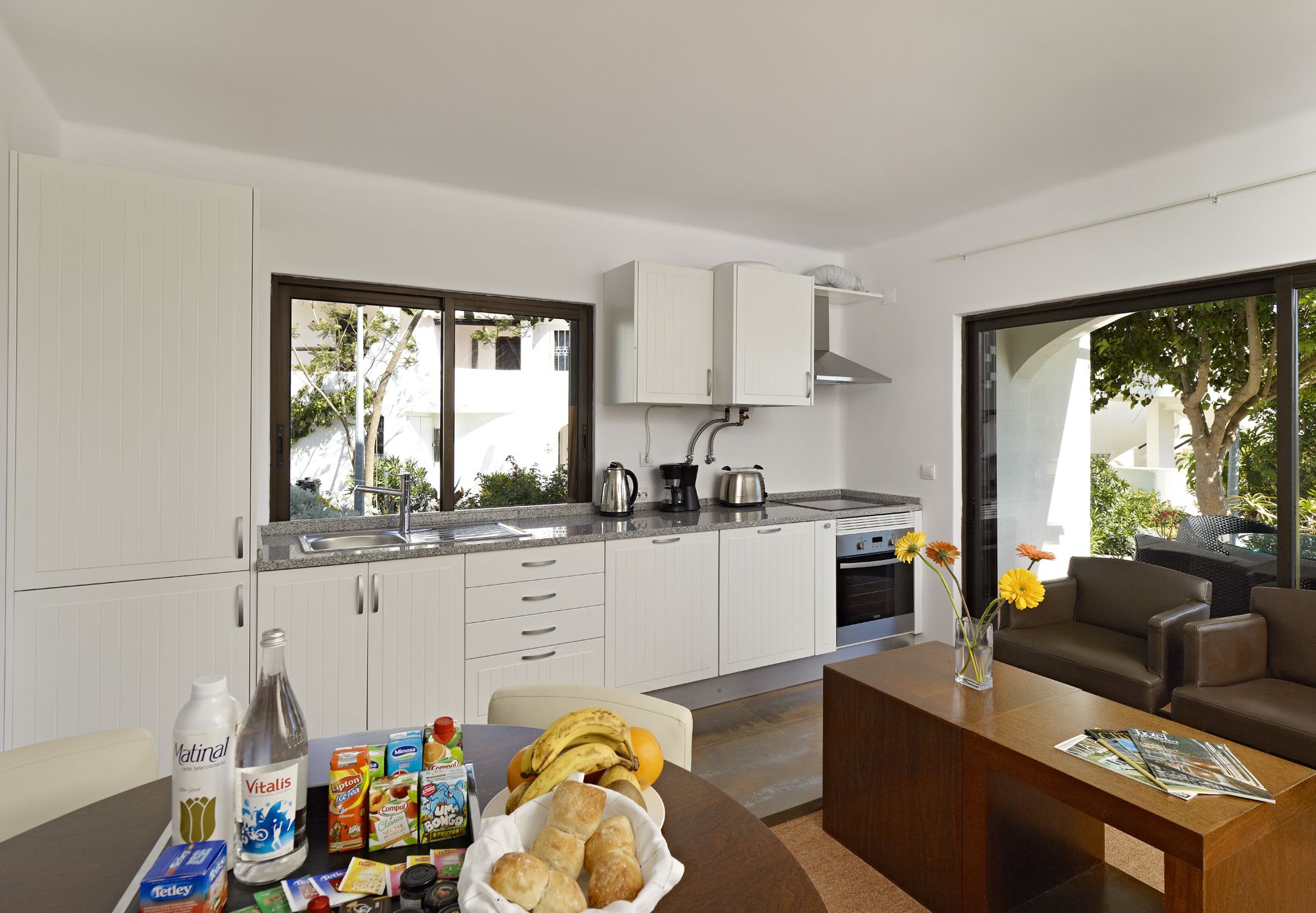 Una cocina moderna con armarios blancos, un comedor con mesa de madera y vistas al exterior.