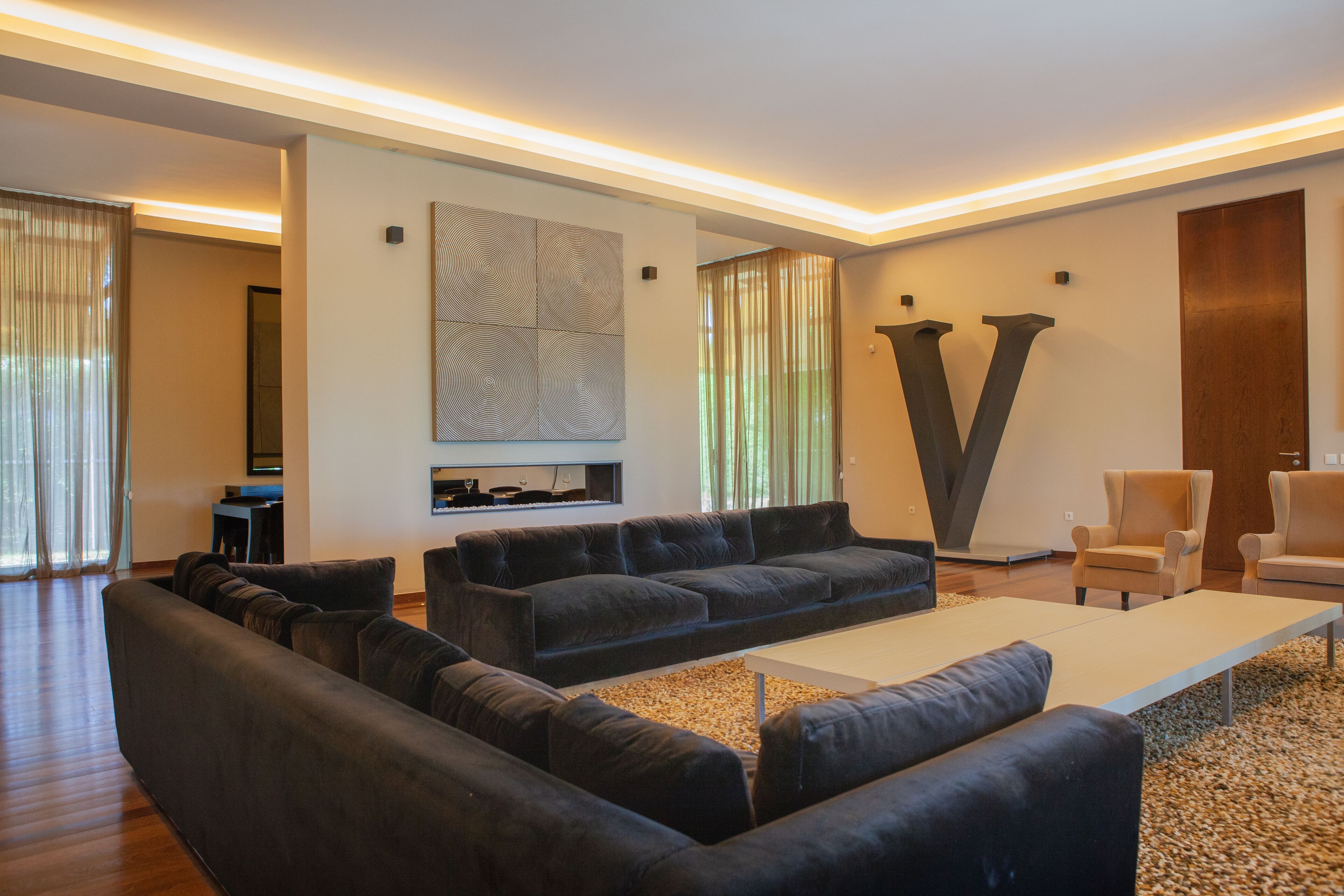 Una sala moderna con un sofá seccional, una mesa de centro y dos sillones. Hay una obra de arte abstracta de gran tamaño en la pared y una chimenea.