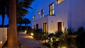A modern building with a cobblestone pathway, palm trees, and outdoor lighting. - São Rafael Holidays (Albufeira)