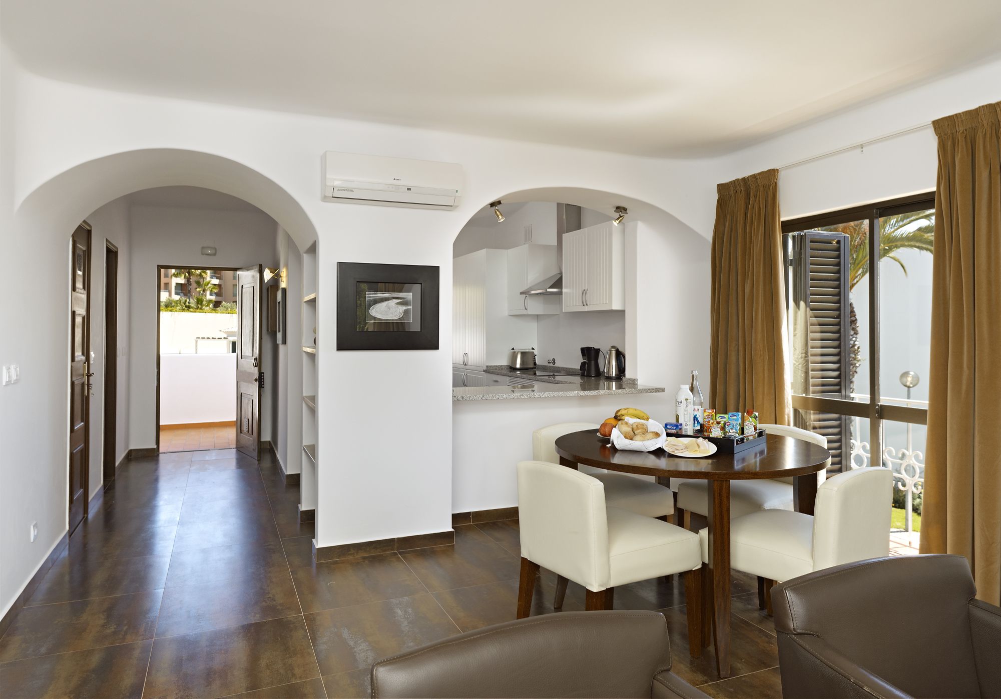 Una cocina moderna con armarios blancos, un comedor con una mesa redonda y sillas, y vistas al exterior a través de un ventanal grande.