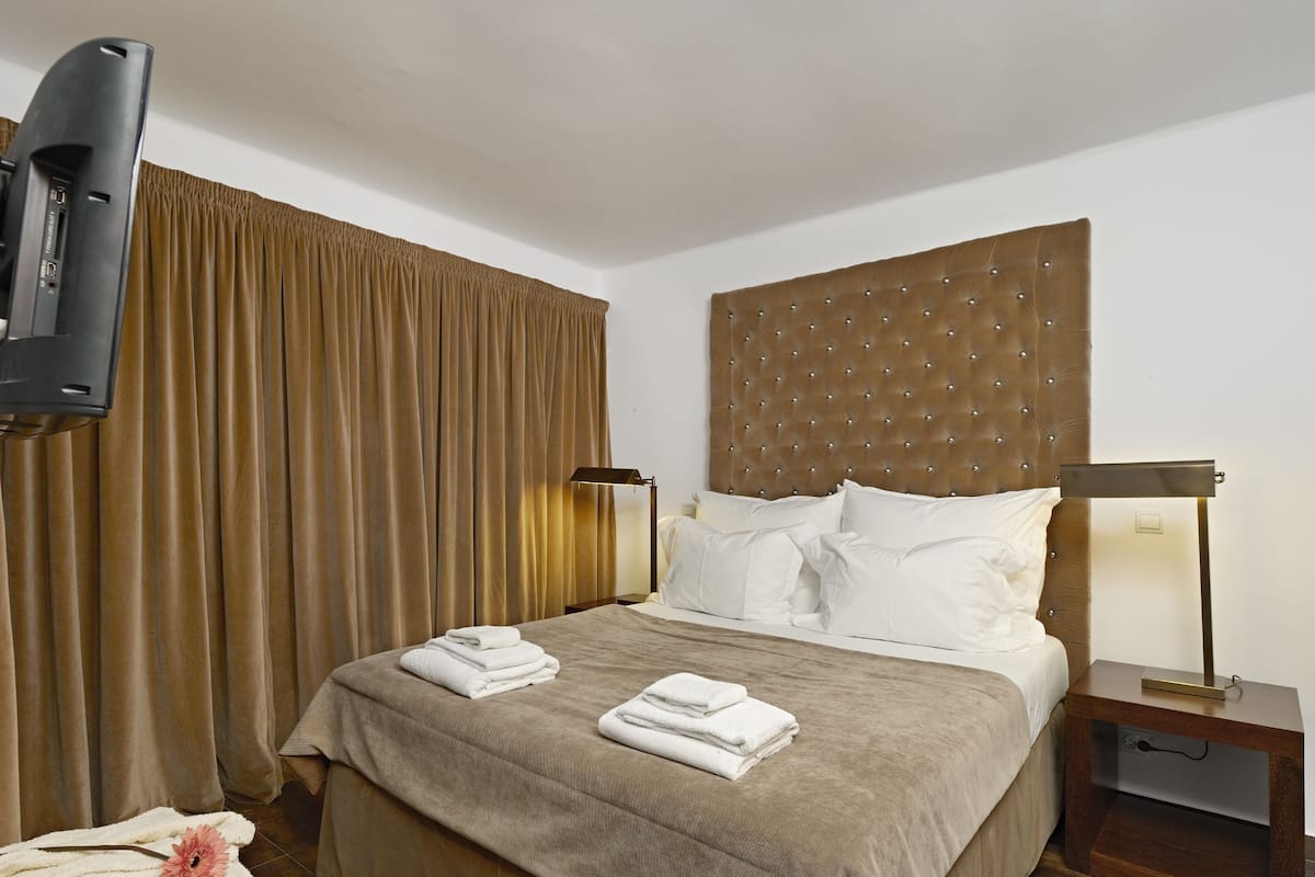 Una habitació d'hotel amb un llit, televisió, cortines i una tauleta de nit amb una làmpada.