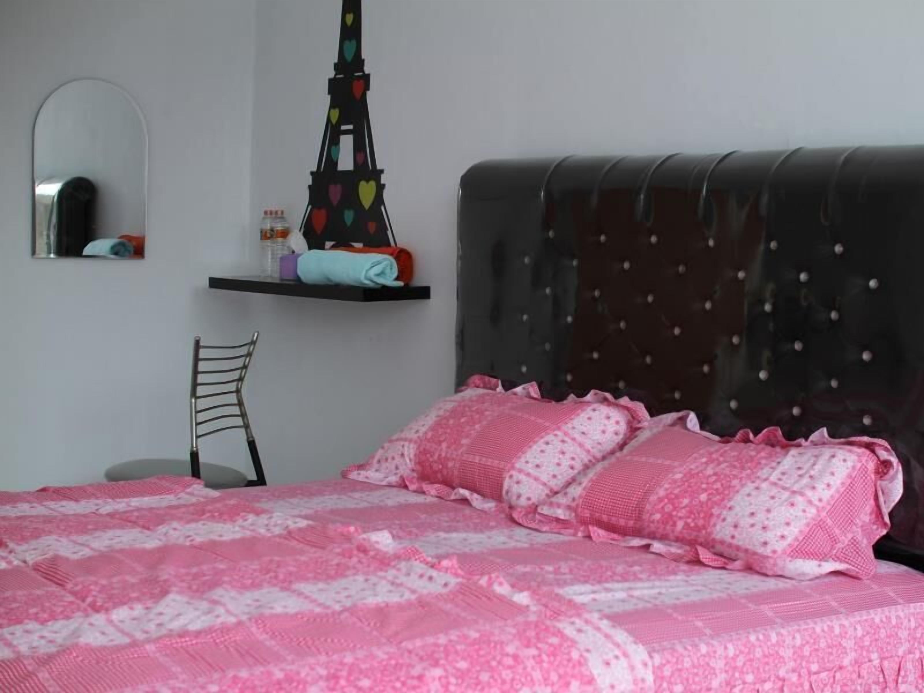 A bedroom with a bed, a chair, a shelf with items, and a mirror.